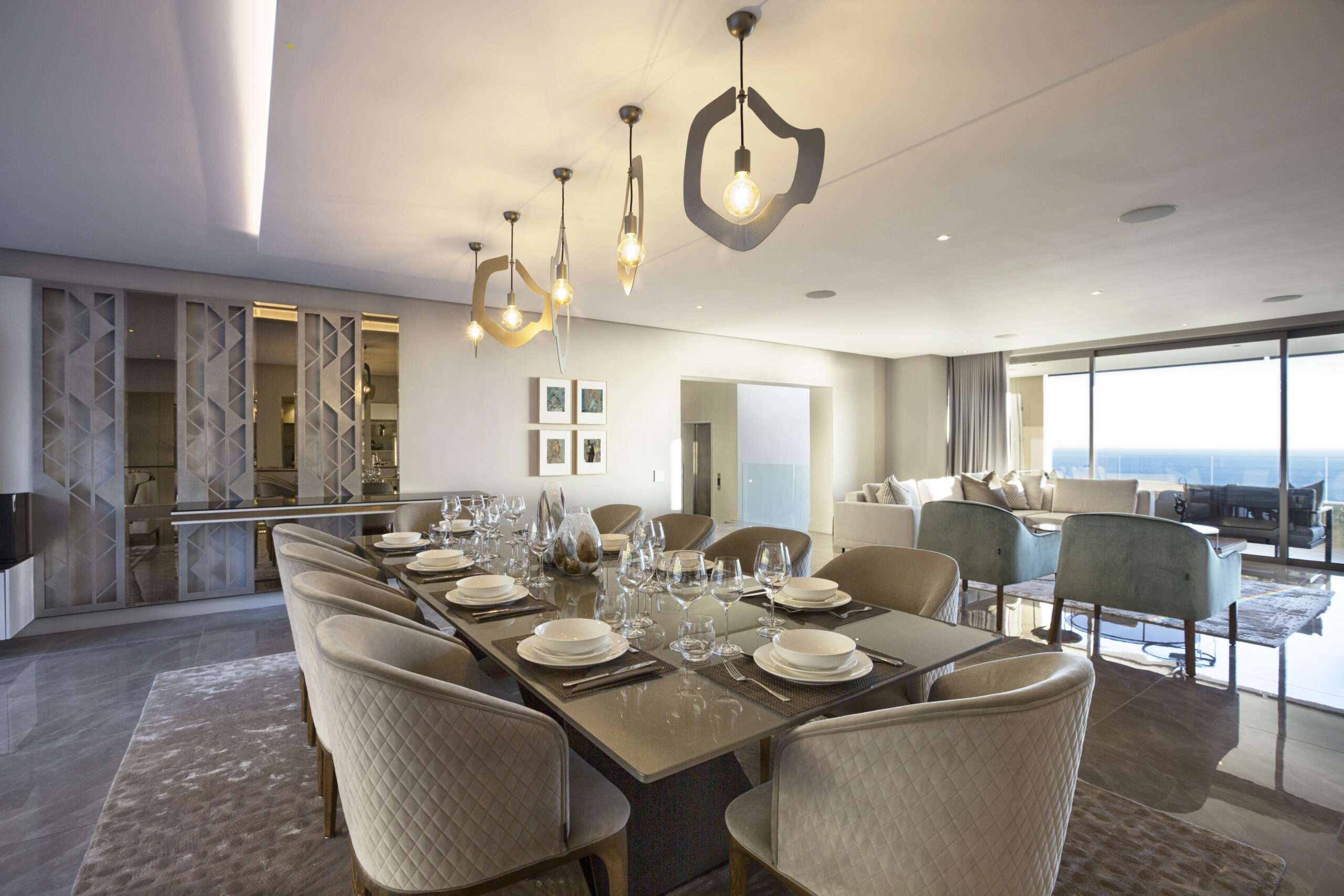 Open-plan dining and living space with a long dining table and floor-to-ceiling glazing facing the sea