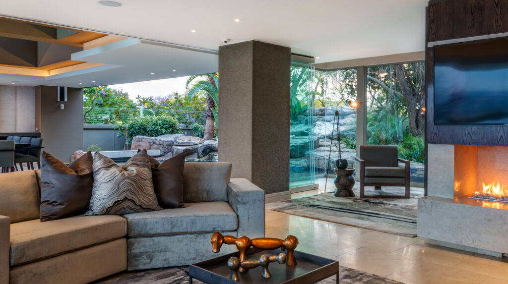 Formal lounge with a velvet sofa, linear fireplace and floor-to-ceiling glass opening onto a rock garden with a water feature