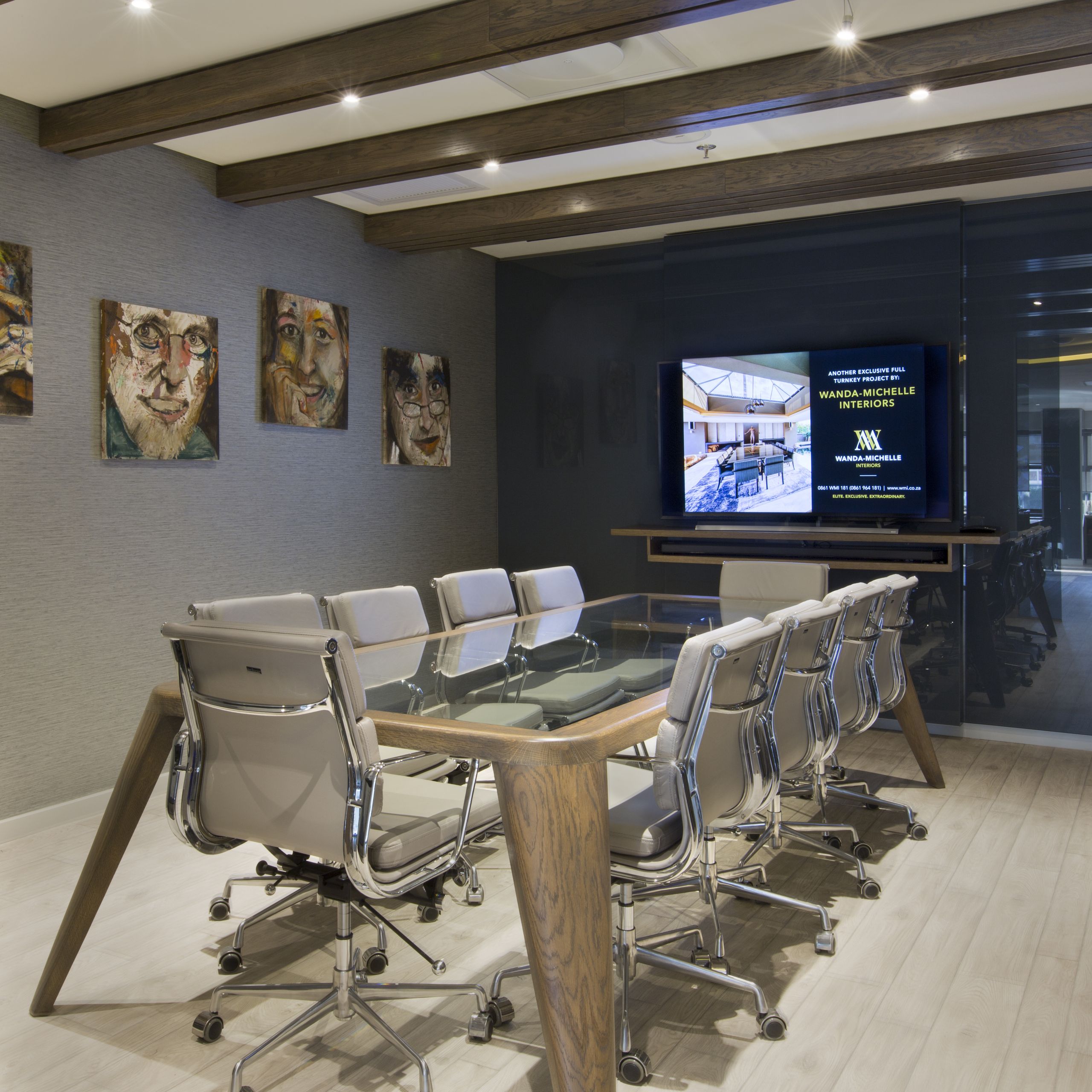 Boardroom with a long timber table, grey task chairs, a wall-mounted screen and framed artworks